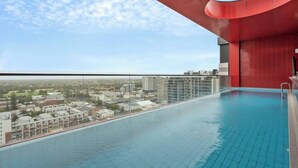 Piscina infinita en la azotea con vista a la ciudad, rodeada de arquitectura roja.
