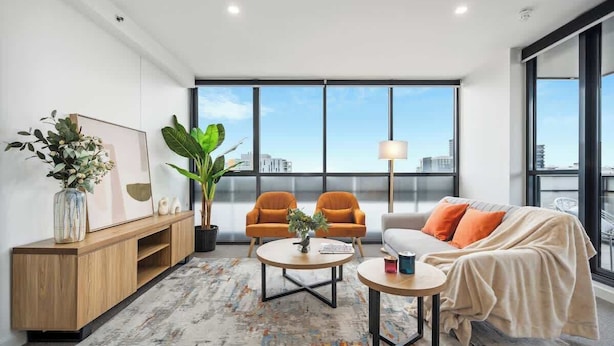 Una sala de estar moderna con un sofá, dos sillones, una mesa de centro, un aparador y un amplio ventanal con vistas a la ciudad.