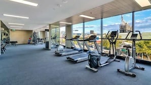 Un gimnasio con cintas de correr y elípticas, amplias ventanas con vista a la ciudad y equipo de ejercicio.
