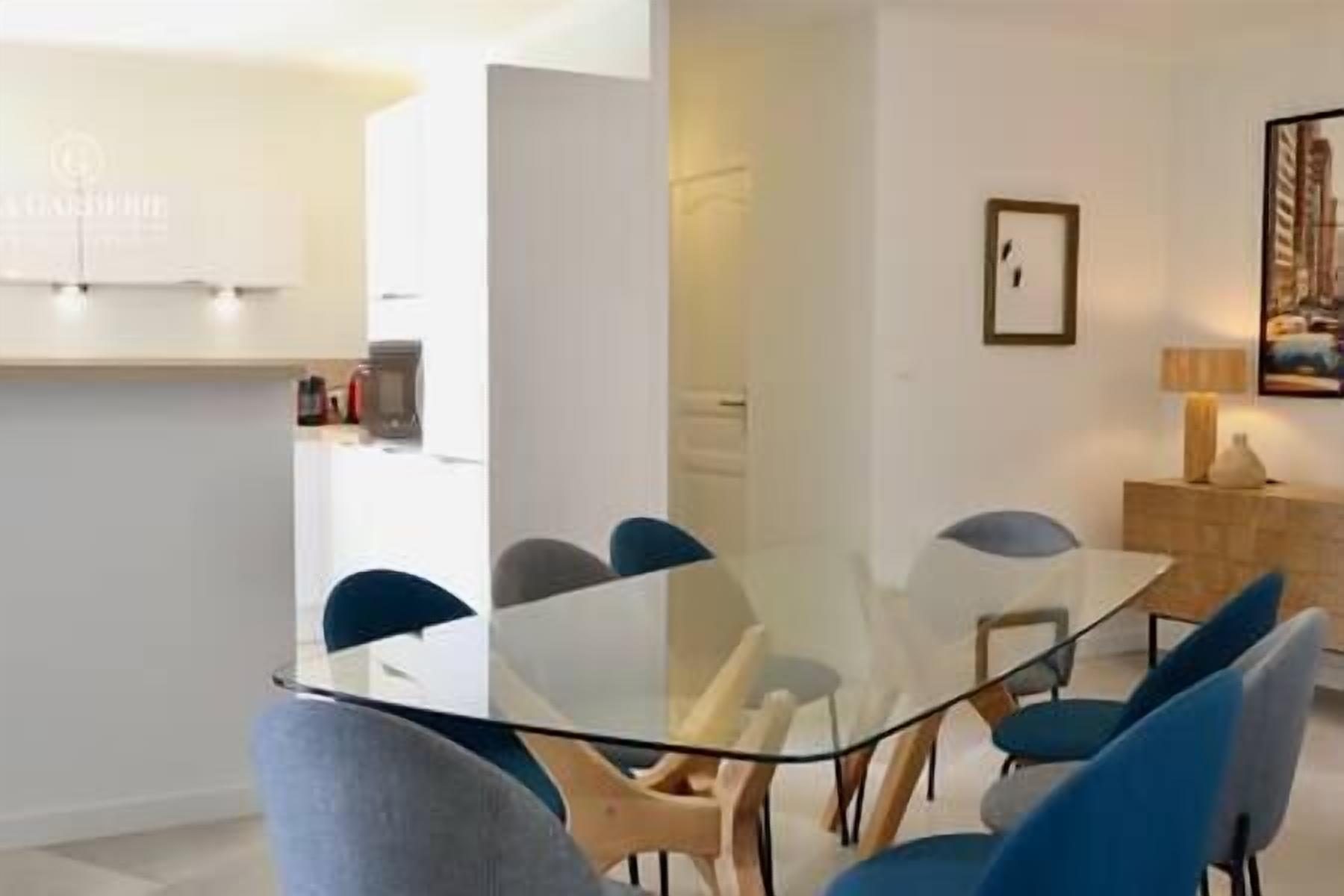 Un espace repas moderne avec une table en verre entourée de chaises bleues, un meuble en bois et un tableau encadré au mur.
