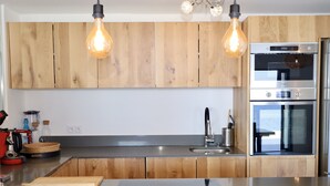 A modern kitchen with wooden cabinets, a stainless steel sink, and two overhead light fixtures. - Maison Dexception les Pieds Dans Leau (Carqueiranne)