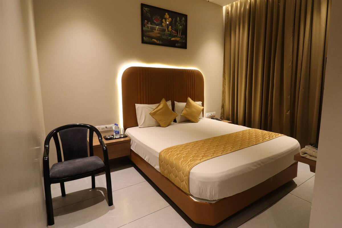 Una habitación de hotel con una cama grande, una silla, una mesita de noche y un cuadro en la pared.