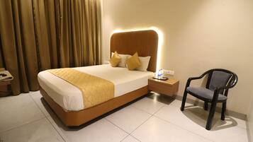 Una habitación de hotel con cama, mesita de noche, silla y cortinas.