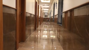 Un long couloir élégant, doté d’un sol brillant, de portes en bois et d’un plafond au design moderne.