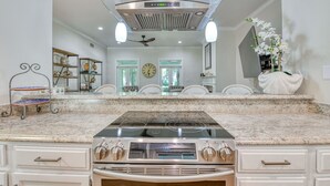 A kitchen with a built-in stove, a large island with seating, and a decorative ceiling vent. - Two-Bedroom, Two-Bath, Single-Story Cottage Located in Wachesaw Plantation (Murrells Inlet)