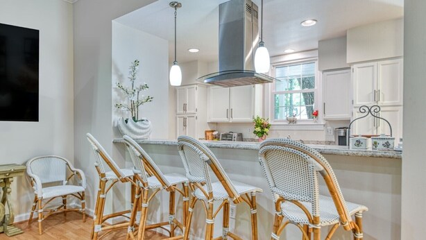 A modern kitchen with white cabinets, a central island with bar stools, and pendant lighting. - Two-Bedroom, Two-Bath, Single-Story Cottage Located in Wachesaw Plantation (Murrells Inlet)