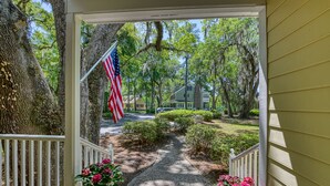 A wooden porch with a white railing, a small garden with pink flowers, and an American flag. - Two-Bedroom, Two-Bath, Single-Story Cottage Located in Wachesaw Plantation (Murrells Inlet)