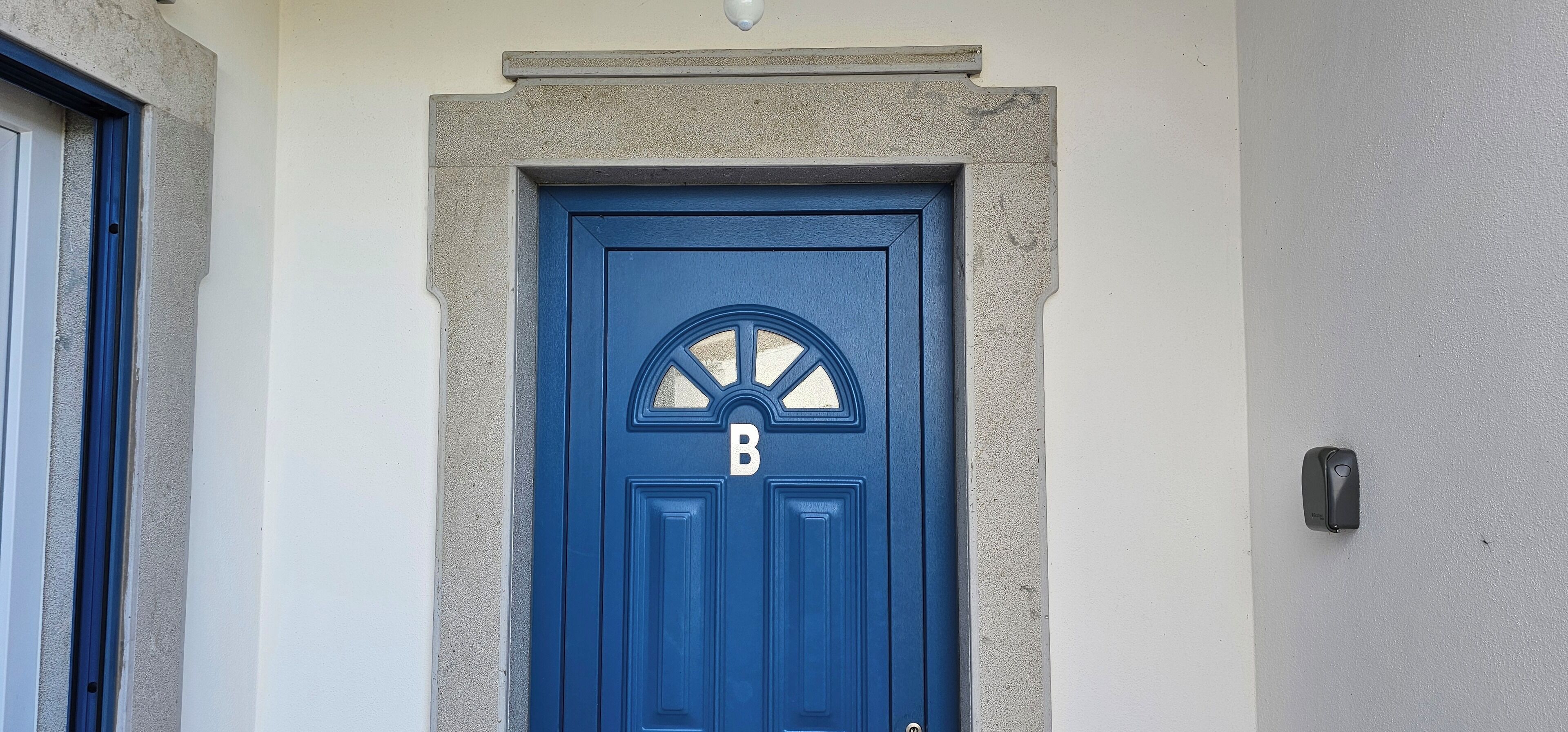Eine blaue Tür mit einem ‘B’ als Kennzeichnung, einem Steinrahmen und einer kleinen Leuchte darüber.