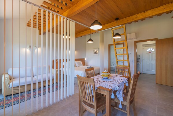 A cozy room with a wooden ceiling, a dining table with chairs, a bed with a white headboard, and a white partition with vertical slats. - Quinta da Bornacha (Vila Real Santo Antonio)
