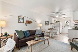 Un salon avec un canapé en cuir marron, une table basse en bois et un coin repas comprenant une table et des chaises blanches.