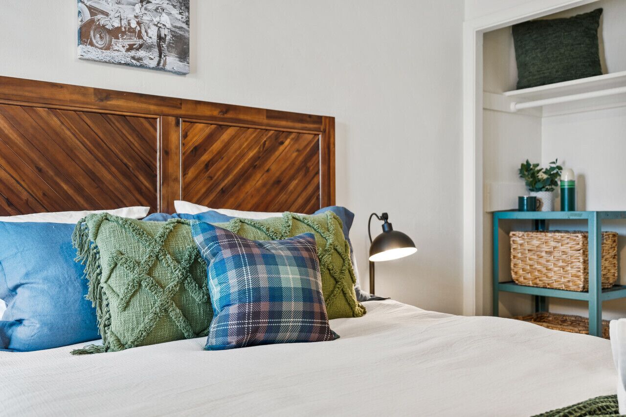 A bed with a wooden headboard, multiple pillows, a bedside lamp, and a shelf with baskets.