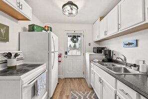Une cuisine de taille réduite avec des meubles blancs, un four à micro-ondes, une cuisinière et un évier.