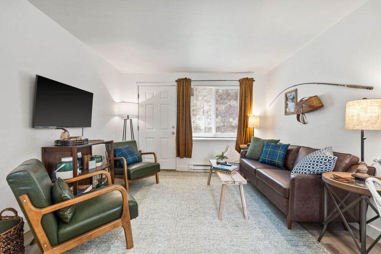 Een woonkamer met een bank, stoelen, een televisie, een lamp en een raam met gordijnen.