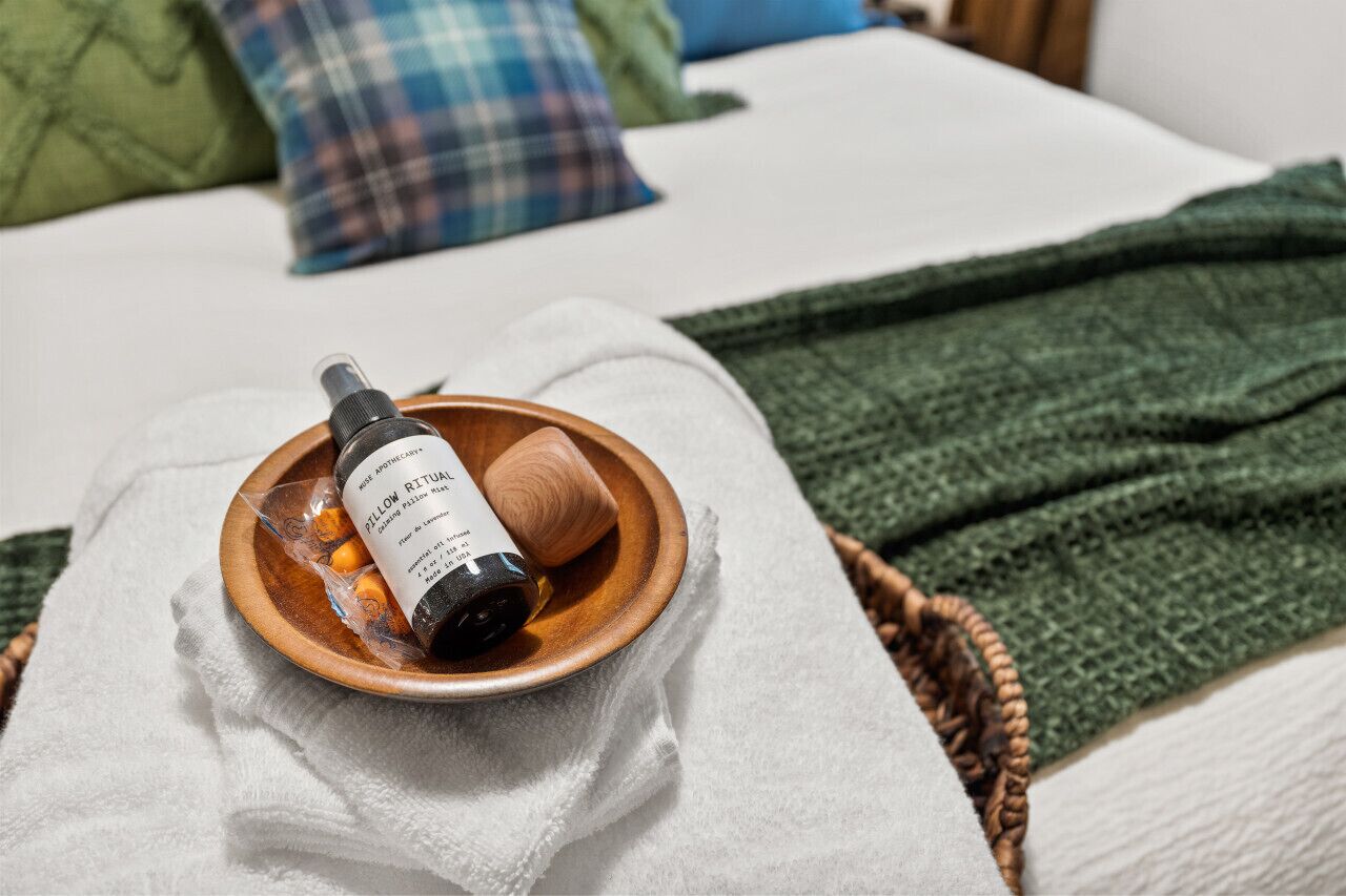 Eine Duftölflasche, eine Holzschale und eine grüne Decke auf einem Bett.