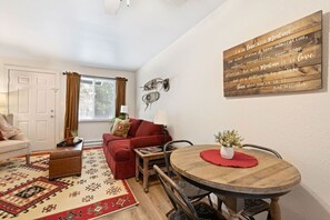A cozy living room with a red sofa, a wooden dining table, and a decorative wall piece. - Charming Apt Near DT Columbia Falls w/ Pickleball (Columbia Falls)