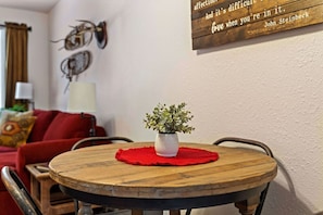 A round wooden table with a red placemat and a white vase with green plants.