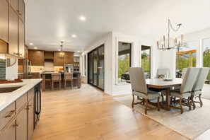 A spacious kitchen with wooden cabinets, a dining area with a table and chairs, and large windows offering a view of the outdoors.