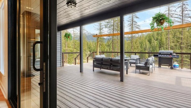 An outdoor deck with a grill, seating, and a view of trees. - Quiet Neighborhood Home w/ Pristine Mountain Views (Kalispell)