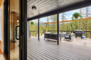 An outdoor deck with a grill, seating, and a view of trees.