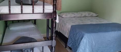 A room with a bunk bed, a single bed, a small round table, and a ceiling fan.