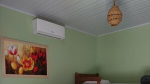 Una habitación con una cama, literas, aire acondicionado instalado en la pared y una lámpara colgante.