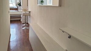 Un couloir doté d’un plancher en bois, d’un mur blanc orné d’un miroir et d’une fenêtre avec des rideaux.