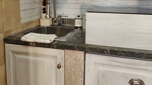 Une cuisine avec des meubles blancs, un plan de travail en granit, un évier en acier inoxydable et un dosseret en briques blanches.