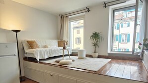 Une chambre à coucher avec un lit, une table de chevet et une fenêtre donnant sur des immeubles.