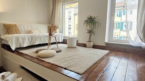 Une chambre moderne avec un lit, un banc et une vue sur la ville grâce à de grandes fenêtres.