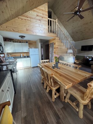 Une cuisine spacieuse de style loft, avec une table et des chaises en bois, un réfrigérateur et un escalier menant à un niveau supérieur.