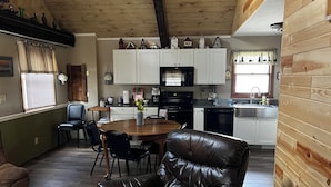 Een gezellig interieur van een chalet met een eethoek, keuken en een leren bank.