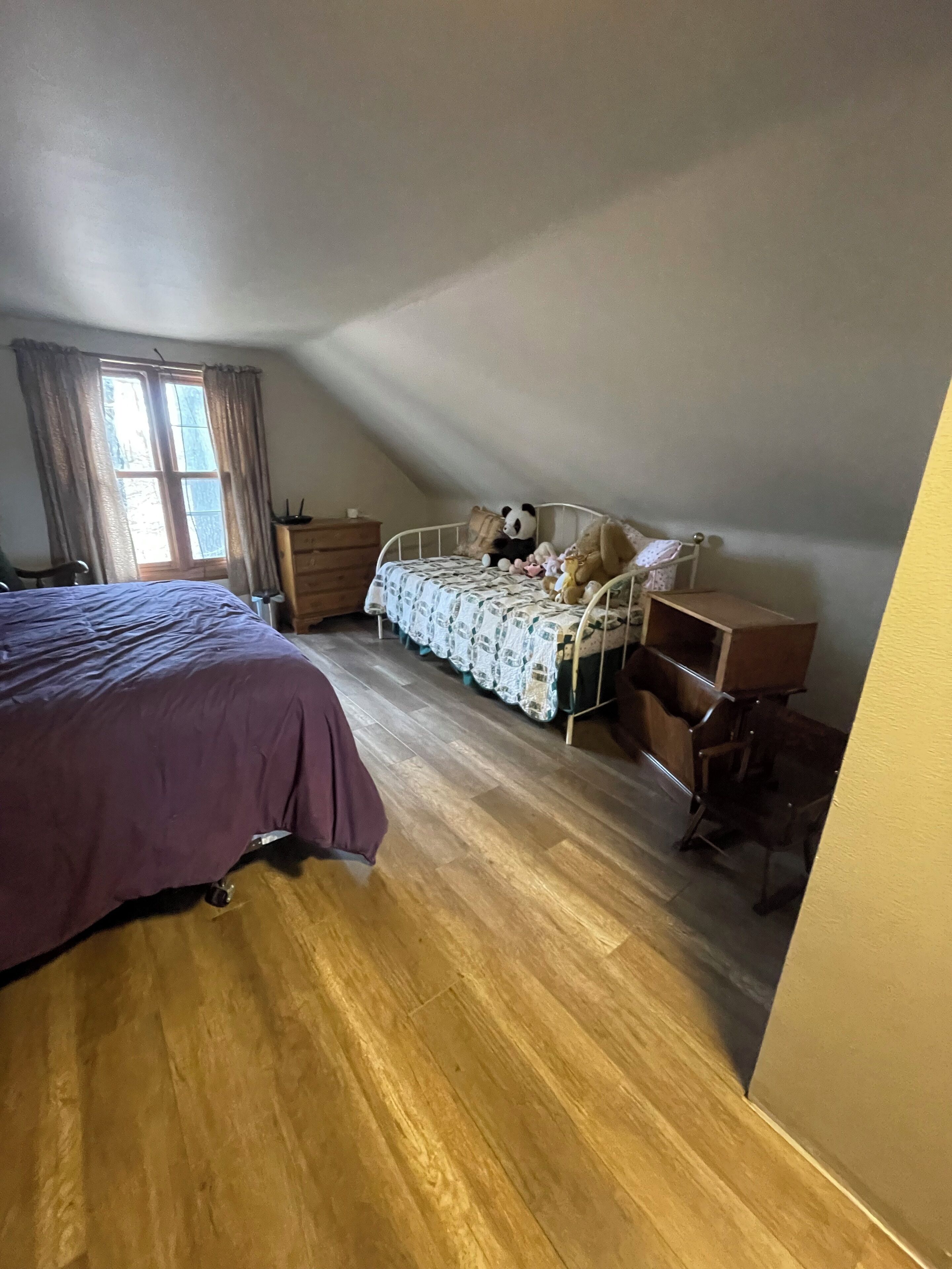 A bedroom with a bed, a desk, a chair, a dresser, and a window with curtains.
