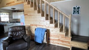 Een houten trap leidt naar een hoger gelegen verdieping, een leren fauteuil en een keukenhoek.