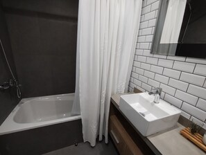 Ett modernt badrum med ett badkar, en vit tvättställ och en spegel.