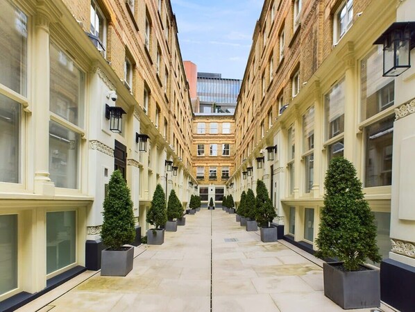 A corridor with symmetrical architecture, featuring a central walkway flanked by buildings with large windows and decorative moldings.