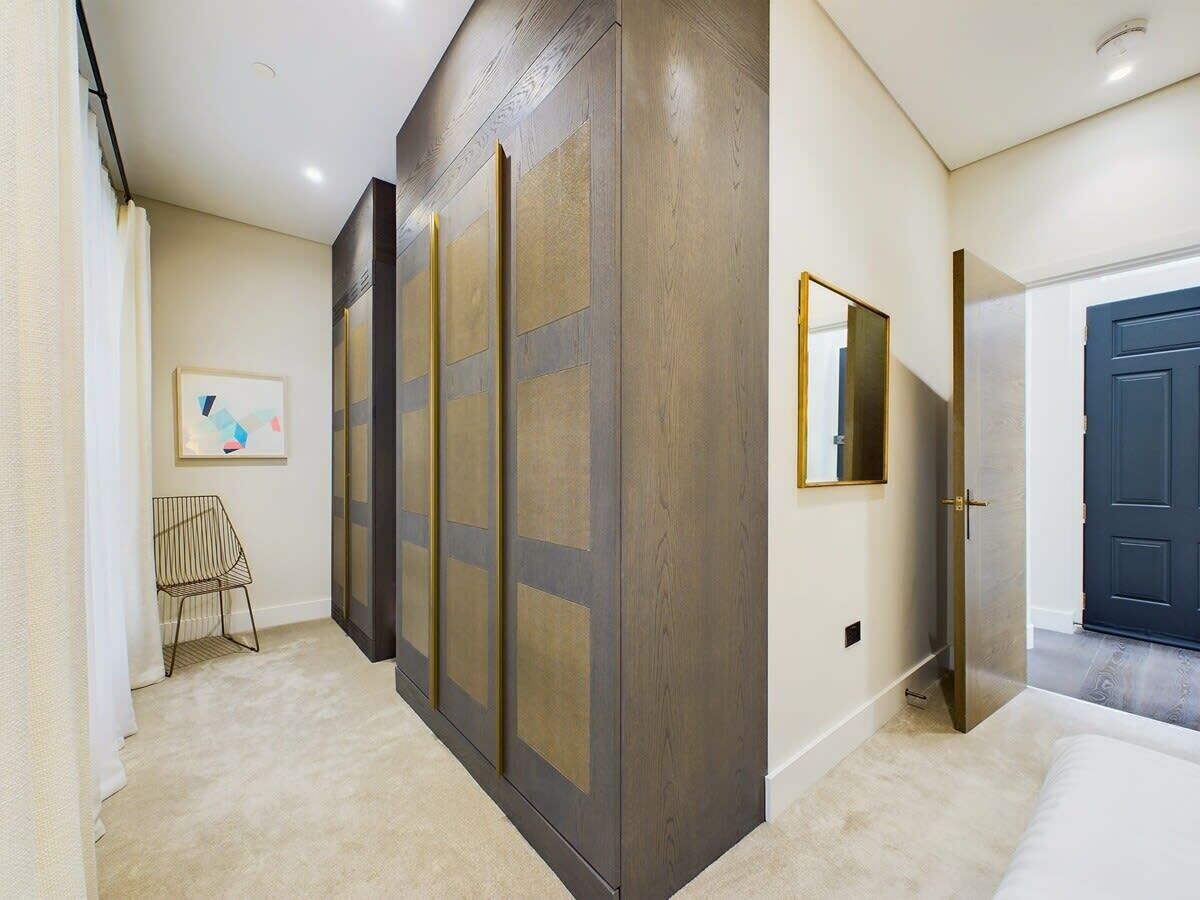 A hallway with a modern design, featuring a large mirror, a framed abstract artwork, and a door leading to another room.