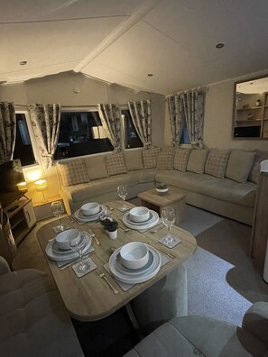 A cozy living area with a dining table set for four, a sofa, and a small side table. - KMH Caravan Holidays (Malton)