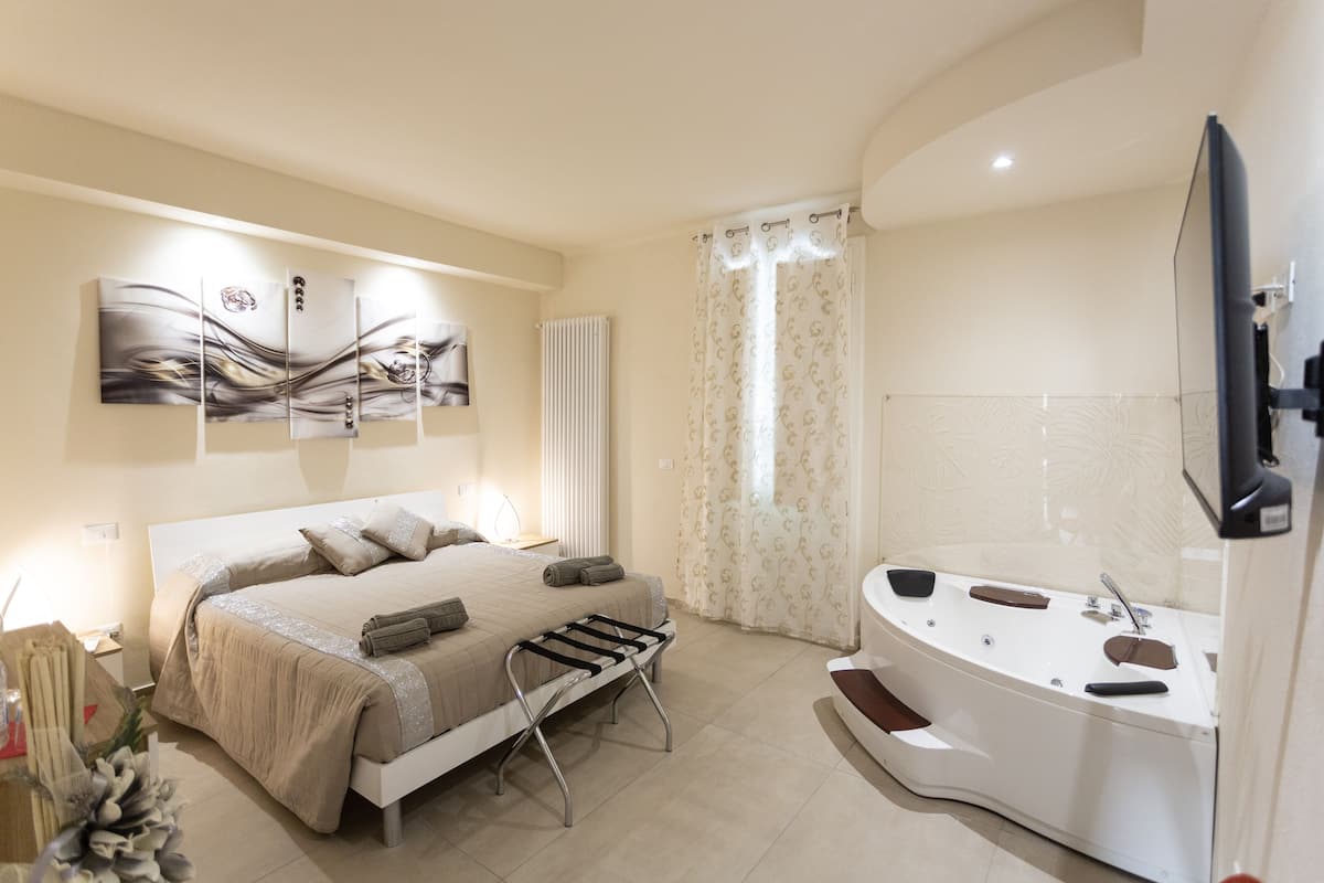 A modern bedroom with a large bed, a built-in bench, a bathtub, and a flat-screen TV.