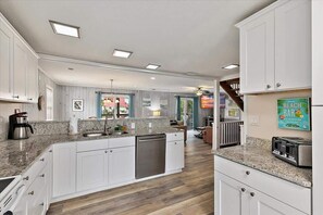A modern kitchen with granite countertops, white cabinetry, and a dishwasher.