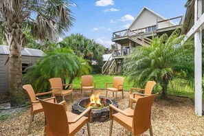 A fire pit with chairs in a garden area, surrounded by palm trees and a building with a balcony.