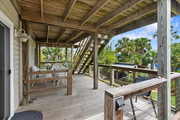 Una terraza de madera con zona de estar cubierta, mobiliario exterior y vistas a palmeras.