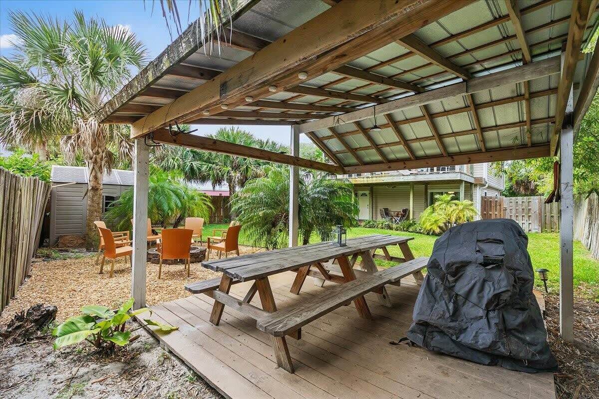 A covered outdoor patio with wooden picnic tables and a barbecue grill.