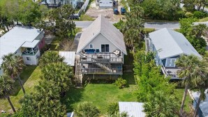 A residential property with a central house featuring a balcony and a covered porch, surrounded by palm trees and other houses.
