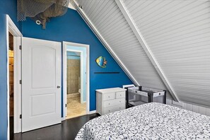 Ein Schlafzimmer mit schrägen Wänden, einem Bett mit gemustertem Bettbezug, einer weißen Kommode und einer Fischdekoration an der Wand.