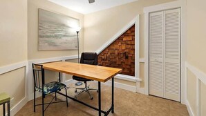 Un petit bureau avec un bureau en bois, une chaise de bureau noire, un ventilateur de plafond, un panneau mural en bois et une armoire blanche.