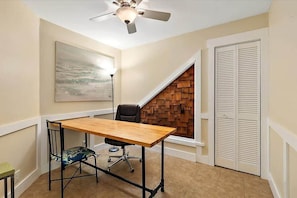 A small office space with a wooden desk, a black office chair, a ceiling fan, a wooden wall panel, and a white closet. - Happy Daze Home, Fire Pit, Gazebo & Vilano Pier (St. Augustine)