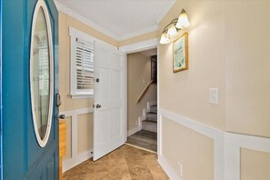 Un pasillo con una puerta azul, una puerta blanca y una escalera que lleva a otra habitación.