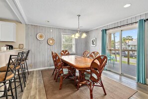 A dining area with a wooden table and chairs, a chandelier, and a view through a sliding glass door. - Happy Daze Home, Fire Pit, Gazebo & Vilano Pier (St. Augustine)
