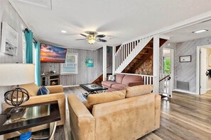 A spacious living room with a fireplace, a large TV, and a staircase leading to an upper level. - Happy Daze Home, Fire Pit, Gazebo & Vilano Pier (St. Augustine)