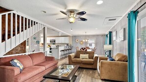 Un vaste salon doté d’un escalier, d’un ventilateur de plafond et offrant une vue sur l’extérieur.